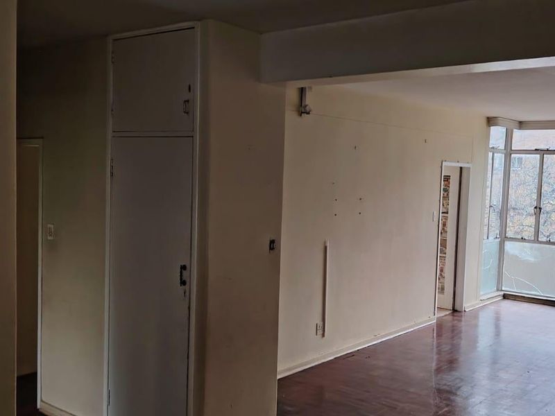 Spacious, empty living area featuring original parquet flooring, built-in storage cupboards, and large windows providing natural light and an elevated view.