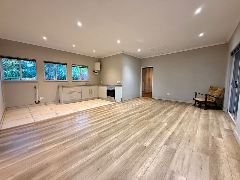 Spacious open-plan living area featuring a functional kitchen with built-in cabinetry, a freestanding oven, and modern laminate flooring throughout.
