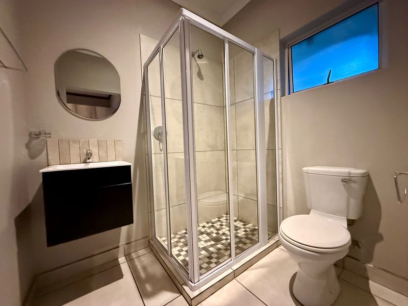 A clean and functional bathroom featuring a glass shower enclosure, wall-mounted vanity with basin, and a standard toilet.