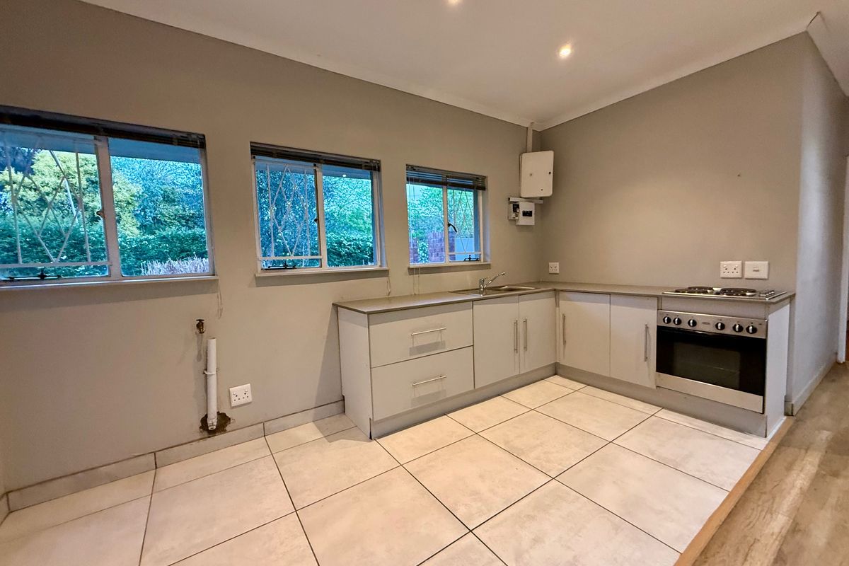 A functional kitchen featuring built-in cabinetry, a stainless steel sink, and a built-in oven with hob, finished with neutral tiled flooring.