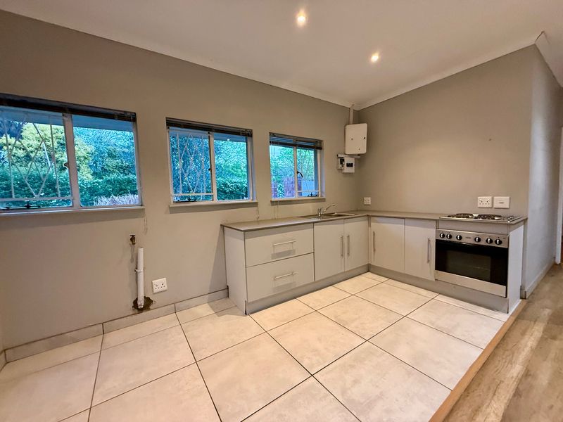 A functional kitchen featuring built-in cabinetry, a stainless steel sink, and a built-in oven with hob, finished with neutral tiled flooring.