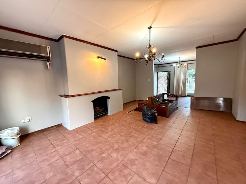 Spacious living room featuring ceramic tile flooring, a built-in fireplace, and a wall-mounted air conditioning unit, offering a versatile layout for comfortable living.