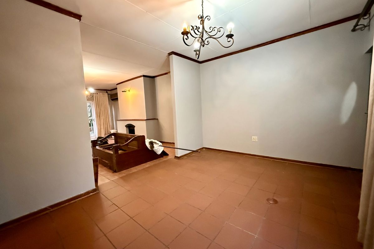 Spacious living area featuring terracotta tiled flooring, a built-in fireplace, and a decorative wrought iron chandelier, offering a blank canvas for renovation.