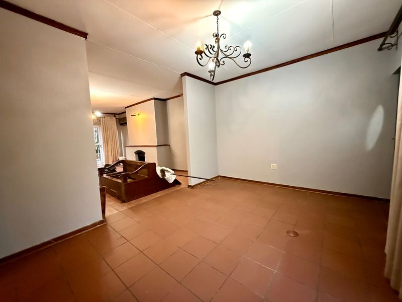 Spacious living area featuring terracotta tiled flooring, a built-in fireplace, and a decorative wrought iron chandelier, offering a blank canvas for renovation.