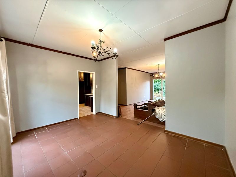 Spacious open-plan living and dining area featuring tiled flooring, wrought iron chandeliers, and direct access to the outdoor space through sliding glass doors.