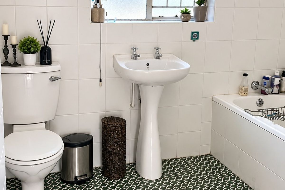 A functional bathroom featuring a pedestal basin, toilet, and bathtub with classic white wall tiling and a decorative patterned floor.