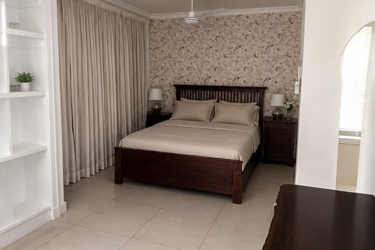 A well-maintained bedroom featuring tiled flooring, built-in shelving, a ceiling fan, and decorative wallpaper, offering a clean and functional living space.