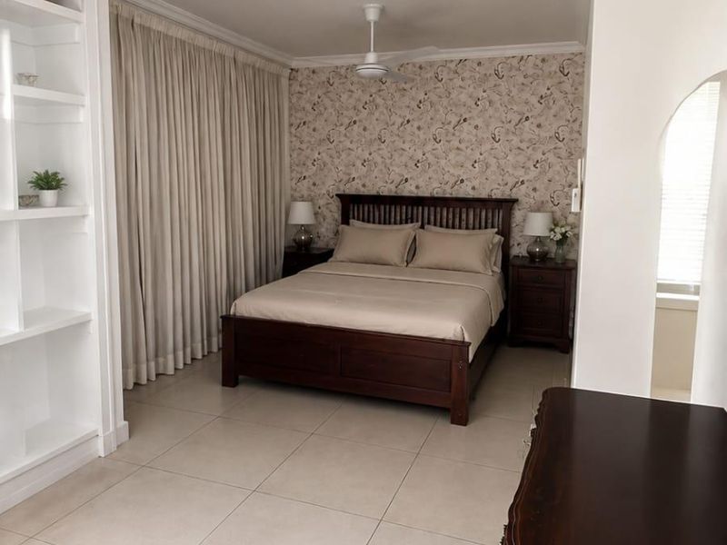A well-maintained bedroom featuring tiled flooring, built-in shelving, a ceiling fan, and decorative wallpaper, offering a clean and functional living space.