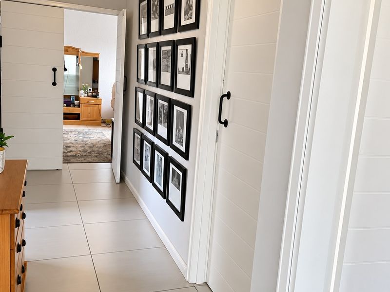 A bright, well-maintained hallway featuring modern tiled flooring, crown molding, and white sliding barn doors.