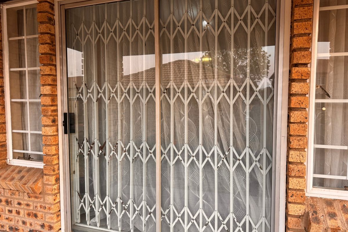 Exterior view of a townhouse featuring a sliding glass door with a security gate and classic face brick exterior walls.