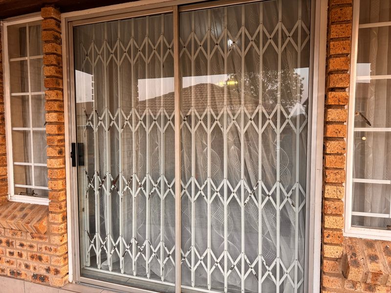 Exterior view of a townhouse featuring a sliding glass door with a security gate and classic face brick exterior walls.
