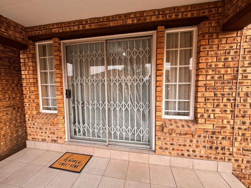 A covered patio area featuring face-brick walls, tiled flooring, and a sliding glass door secured with a metal security gate.