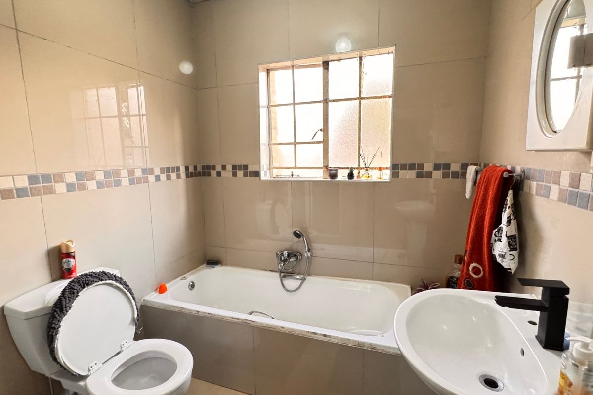 A functional bathroom featuring a bathtub, pedestal basin, and toilet, finished with neutral wall tiles and a decorative mosaic border.