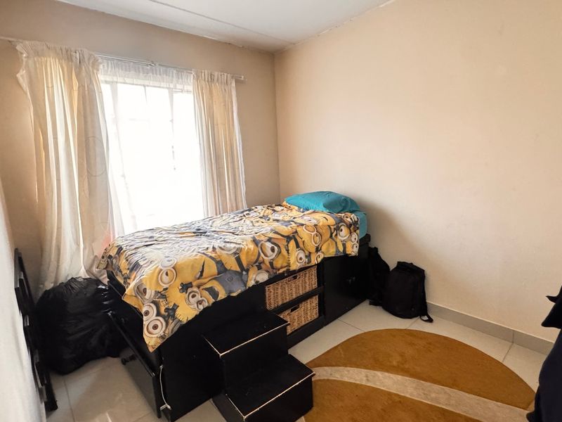 A compact bedroom featuring tiled flooring and a window, providing a functional space for a single bed.