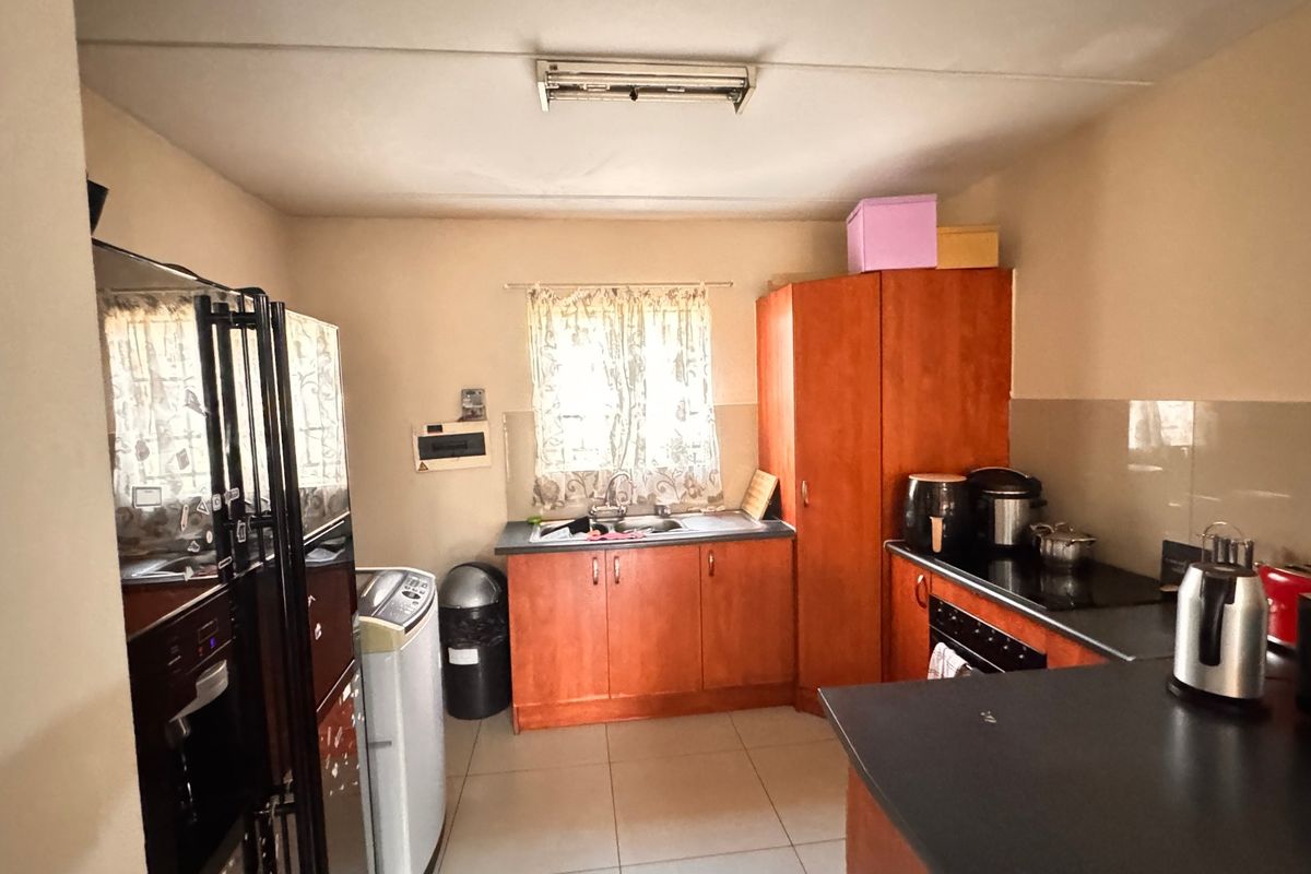A functional kitchen featuring built-in wooden cabinetry, laminate countertops, a stainless steel sink, and integrated oven and hob with tiled flooring.