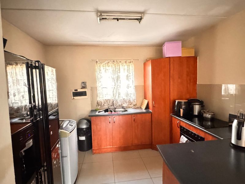 A functional kitchen featuring built-in wooden cabinetry, laminate countertops, a stainless steel sink, and integrated oven and hob with tiled flooring.