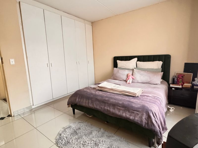 A bedroom featuring tiled flooring and floor-to-ceiling built-in cupboards, with an adjacent view into a bathroom area.