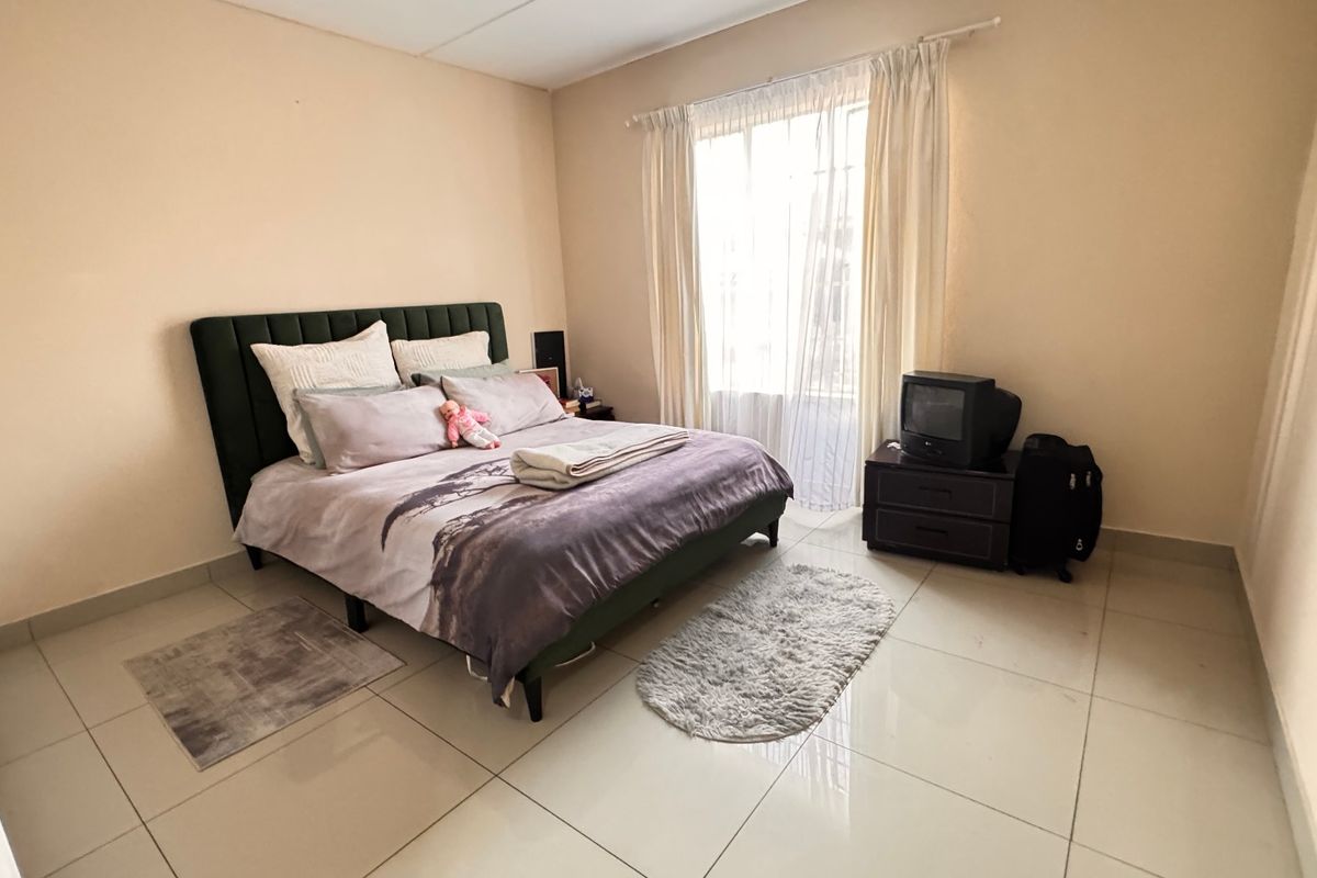 A spacious bedroom featuring neutral wall tones and large format floor tiles, providing a clean and functional foundation for personal styling.