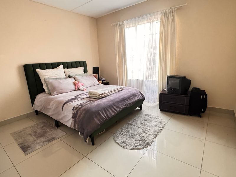 A spacious bedroom featuring neutral wall tones and large format floor tiles, providing a clean and functional foundation for personal styling.