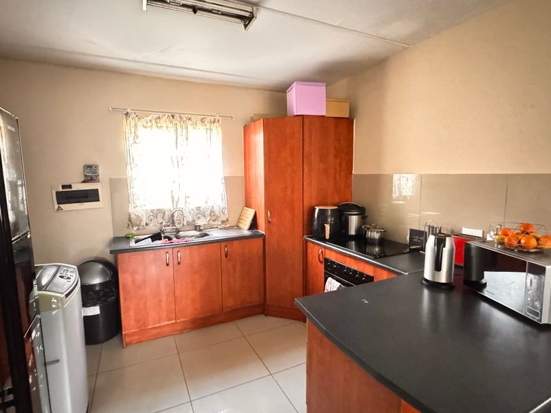 A functional kitchen featuring wood-look cabinetry, dark laminate countertops, tiled splashbacks, and integrated cooking appliances with tiled flooring throughout.