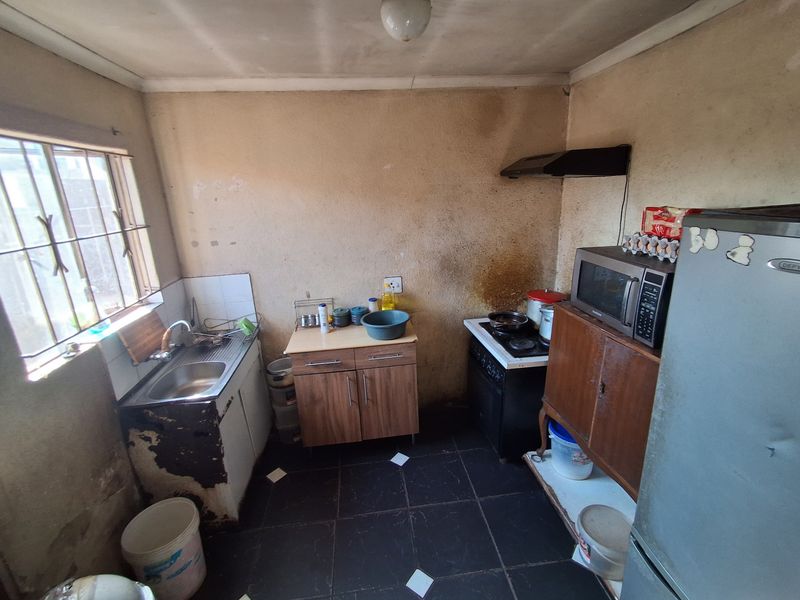 A compact kitchen featuring tiled flooring, a stainless steel sink, and built-in cabinetry, currently requiring significant cosmetic renovation and wall surface repairs.