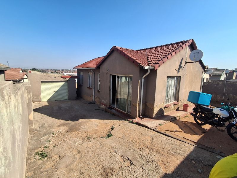 Rear view of a detached house featuring a tiled roof, sliding door access, and a concrete driveway with an attached garage.