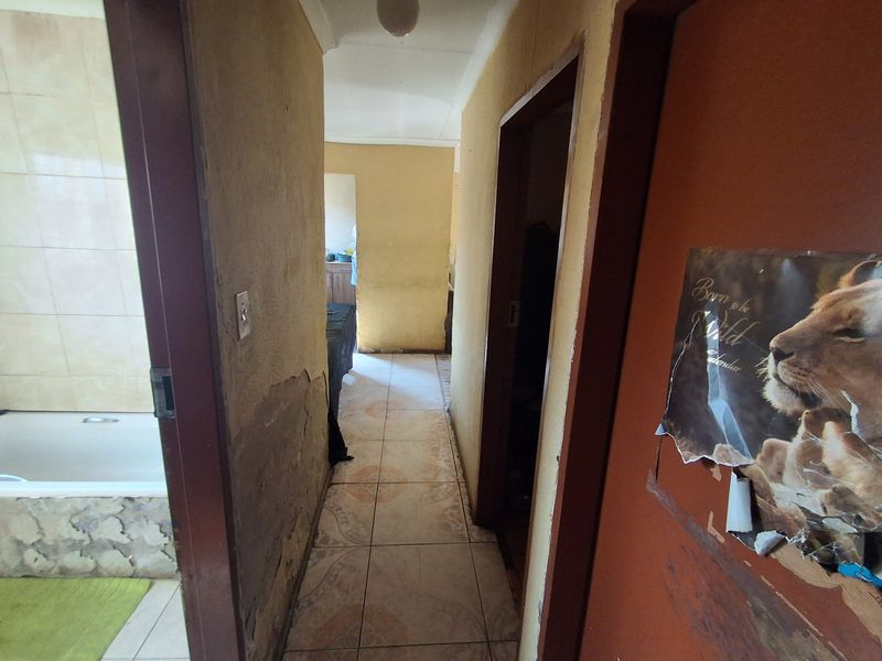 A narrow hallway with tiled flooring leading to a bathroom area, showing significant wear and damage to the wall finishes.