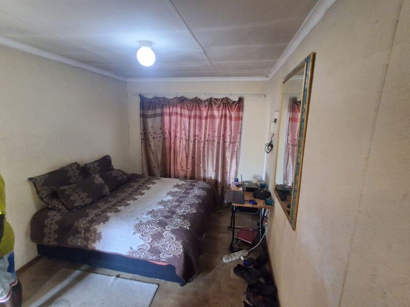 A compact bedroom featuring neutral wall finishes, a ceiling light fixture, and a window with curtain rod installation.