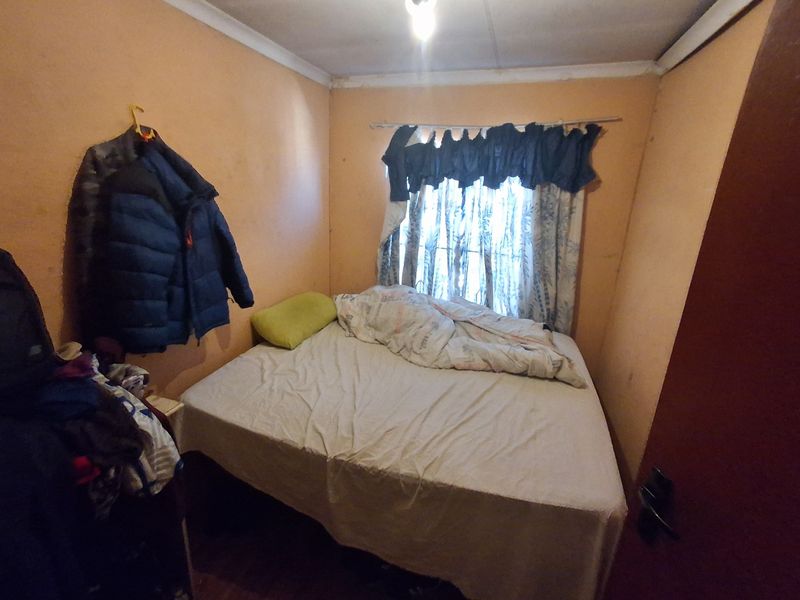 A compact bedroom featuring plain walls and a window with a curtain rod, requiring cosmetic updates to improve the overall finish.