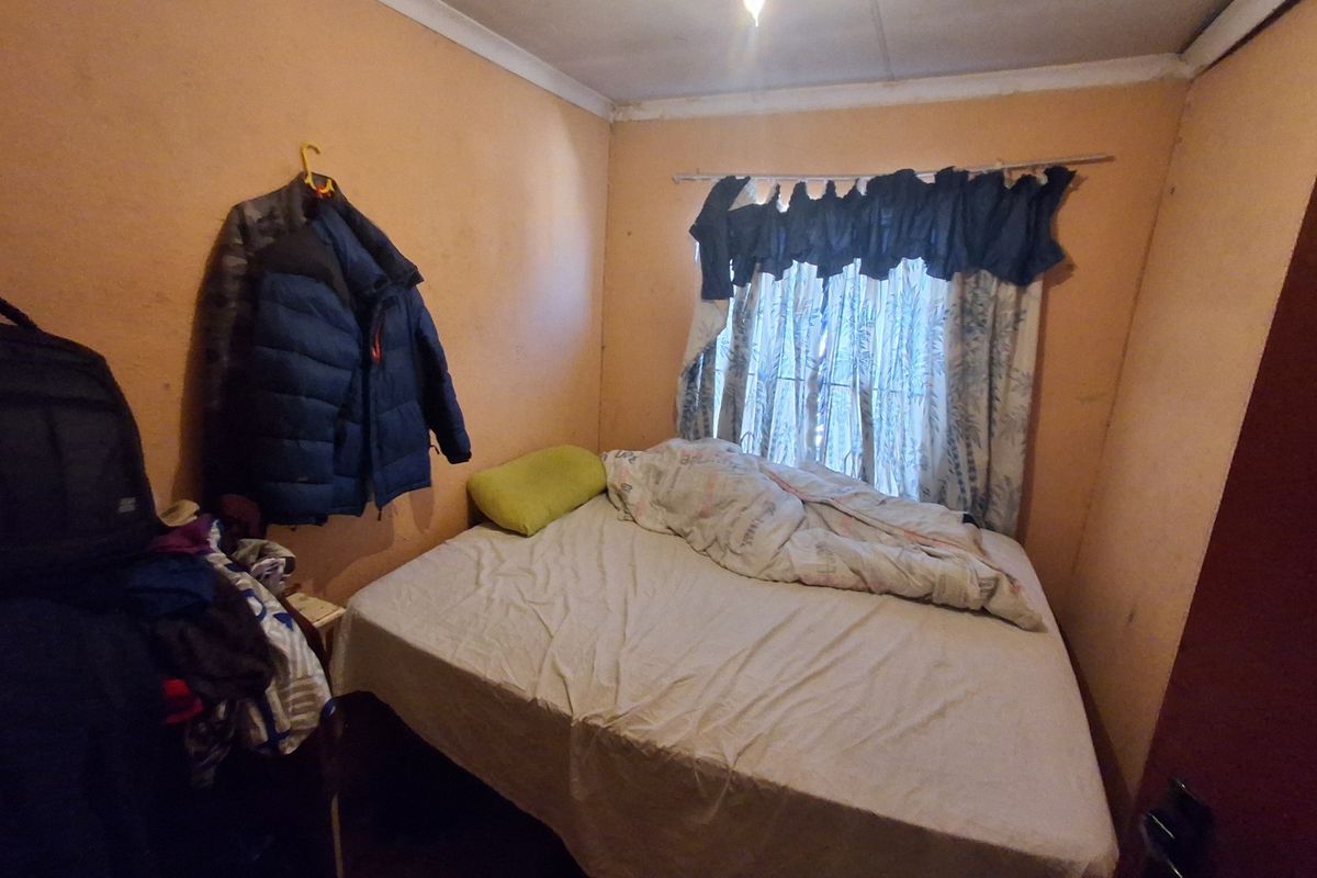 A compact bedroom featuring plain walls and a window with a curtain rod, requiring cosmetic updates to improve the overall aesthetic.