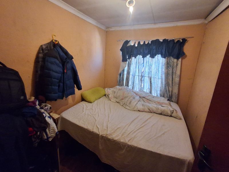A compact bedroom featuring plain walls and a window with a curtain rod, requiring cosmetic updates to improve the overall aesthetic.