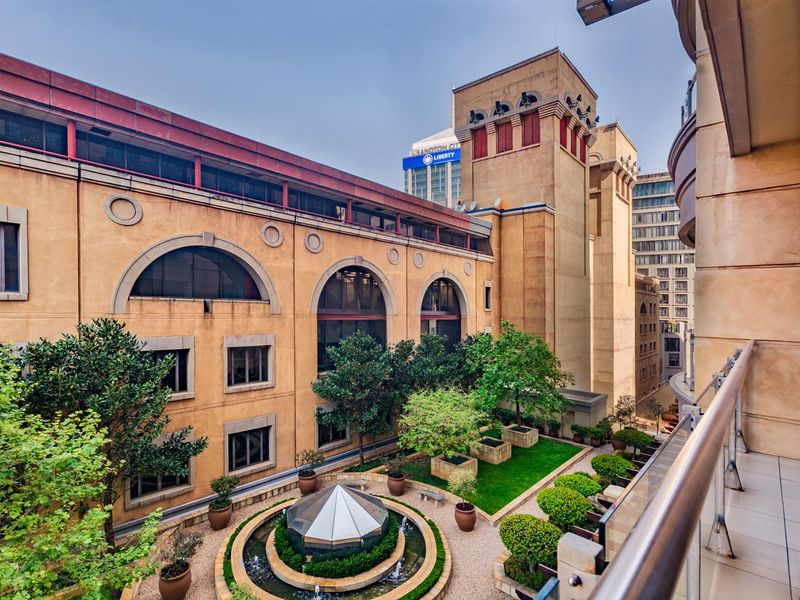 A high-angle view overlooking a well-maintained landscaped courtyard with a central water feature, framed by the building's stone facade and a balcony railing.