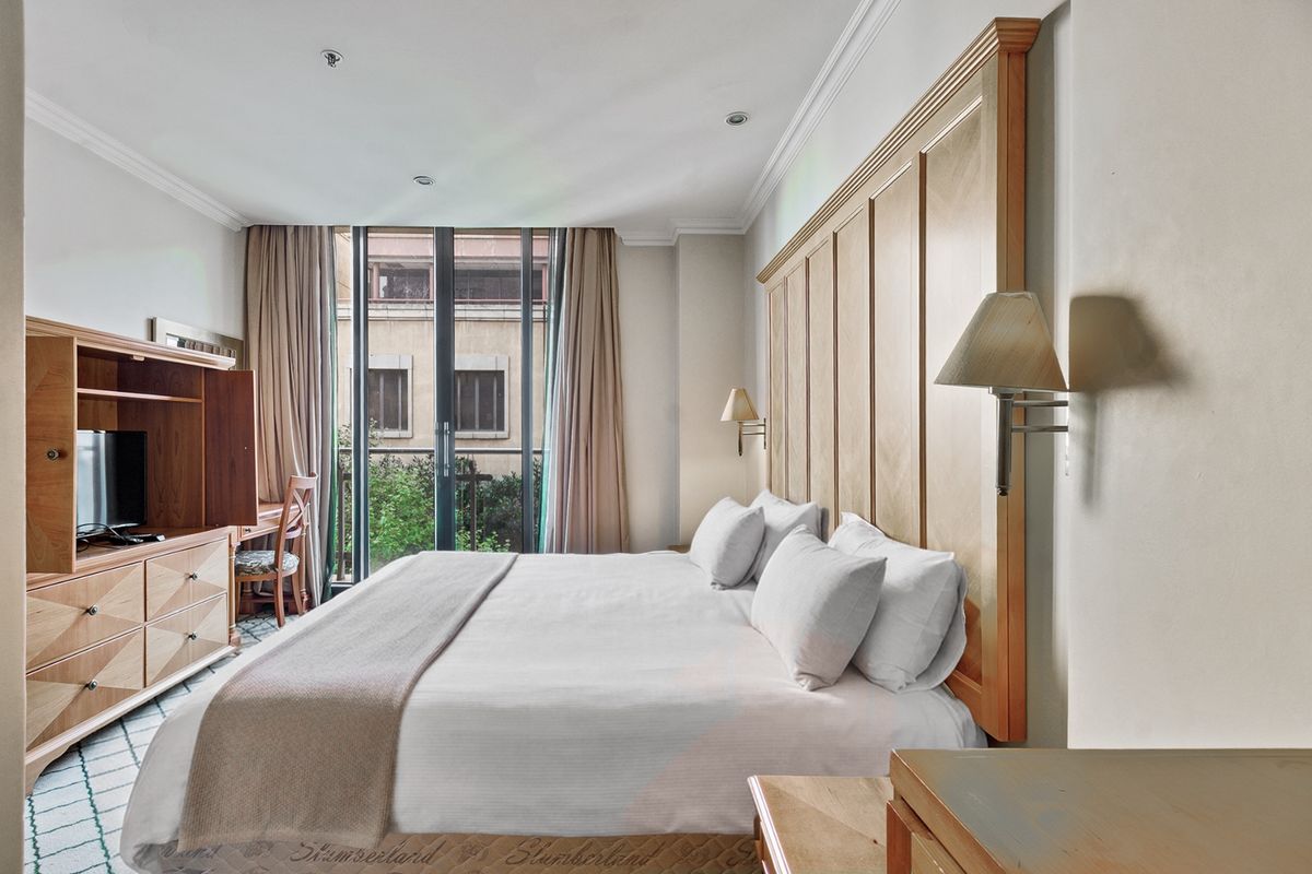 A well-maintained bedroom featuring a large built-in wooden headboard, recessed lighting, and direct access to a private balcony through sliding glass doors.