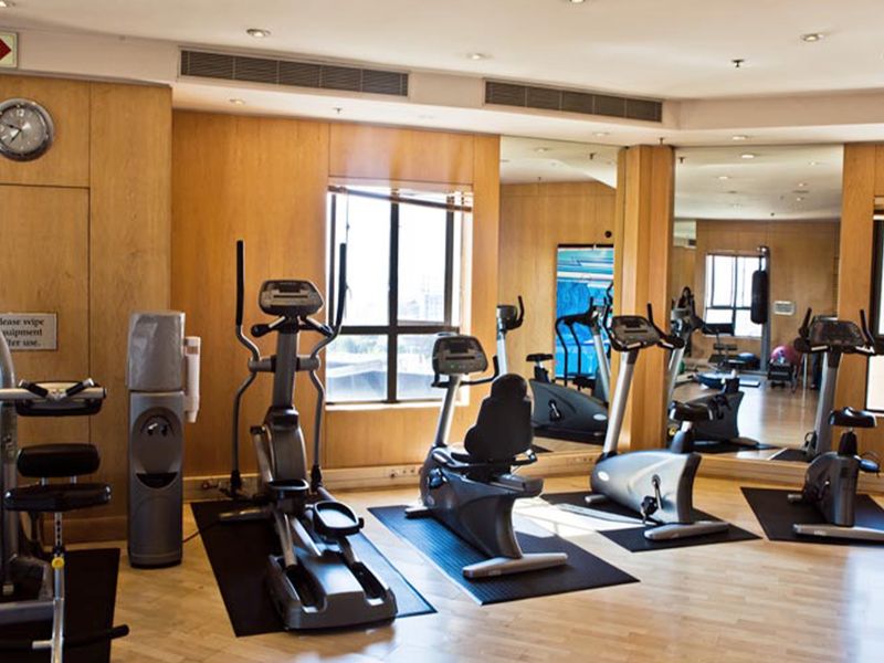 A well-maintained apartment complex gym featuring wood-paneled walls, large mirrors, recessed lighting, and ducted air conditioning for a comfortable workout environment.