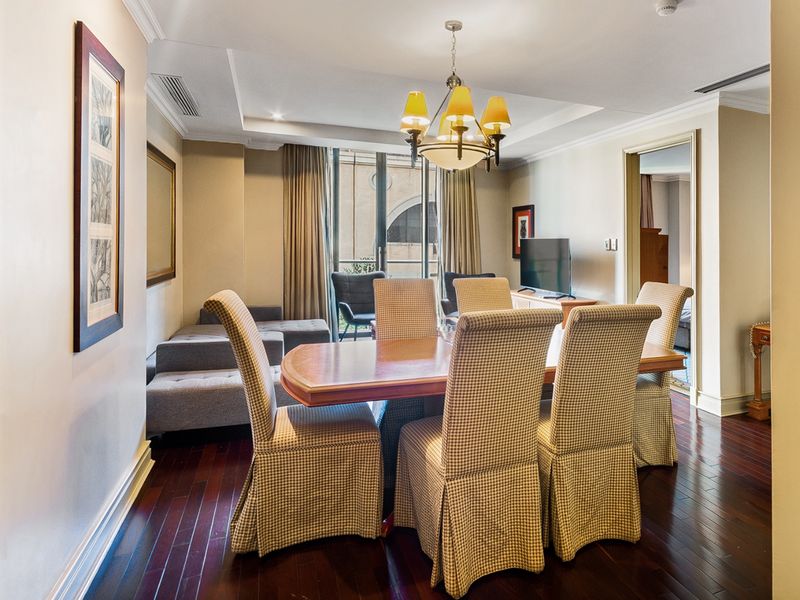 A well-maintained dining area featuring rich hardwood flooring, a decorative chandelier, and a recessed ceiling, with direct access to a balcony.