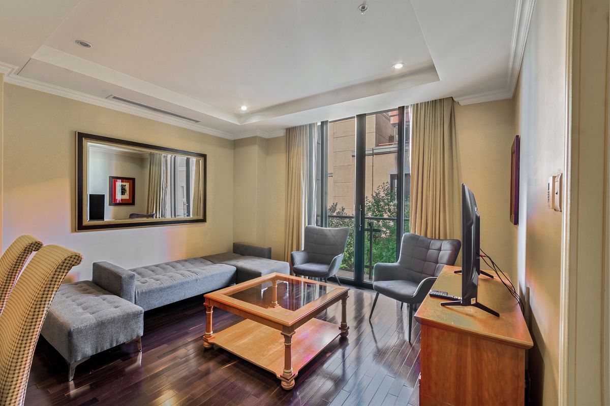 A well-lit living room featuring dark hardwood flooring, a recessed ceiling with cove lighting, and a sliding glass door leading to a balcony.