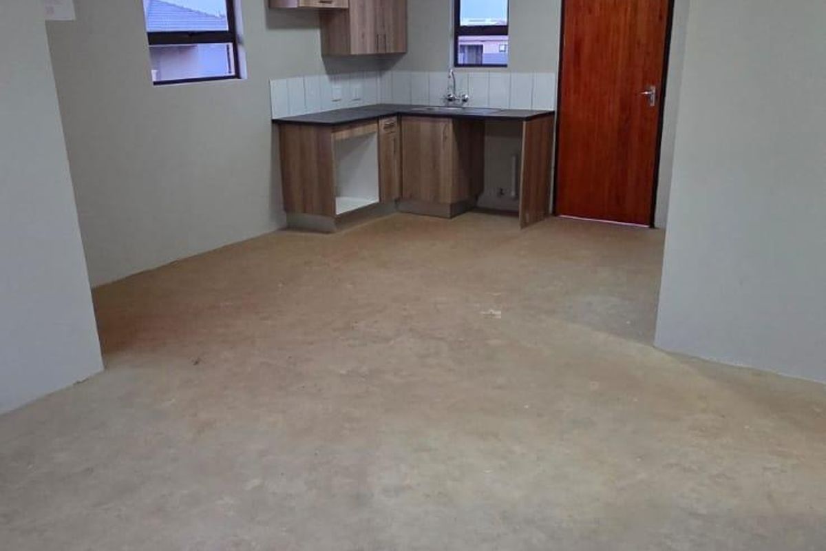 Open plan kitchen area featuring basic cabinetry, sink, and tiled splashback, currently awaiting final flooring installation.