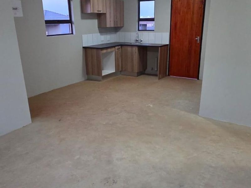 Open plan kitchen area featuring basic cabinetry, sink, and tiled splashback, currently awaiting final flooring installation.