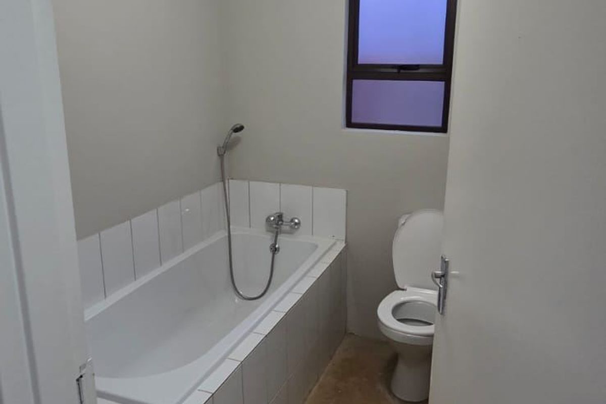 A functional bathroom featuring a built-in bathtub with tiled surround and a standard toilet, awaiting final flooring installation.
