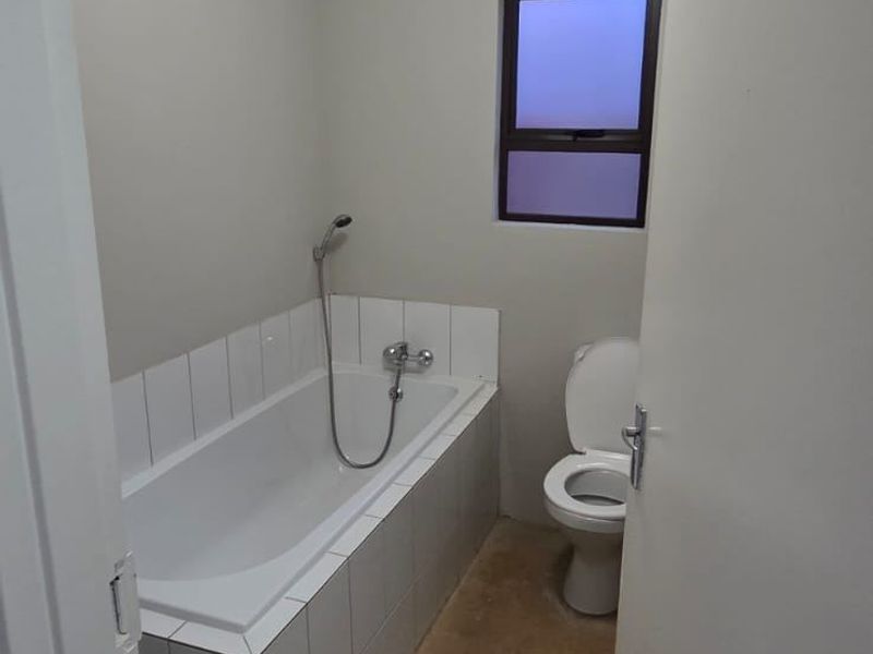 A functional bathroom featuring a built-in bathtub with tiled surround and a standard toilet, awaiting final flooring installation.