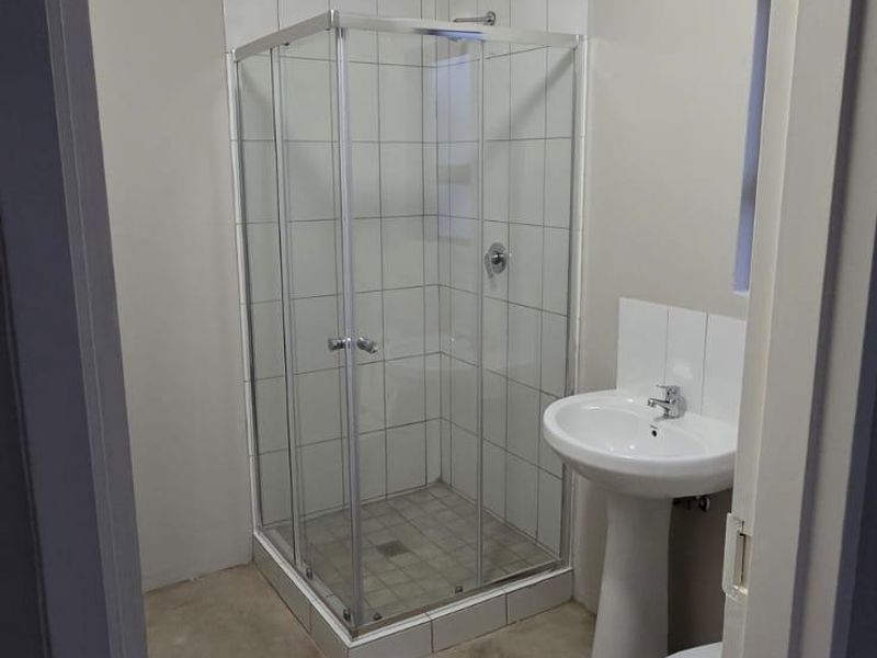 A functional bathroom featuring a shower enclosure, pedestal basin, and toilet, currently awaiting final flooring installation.