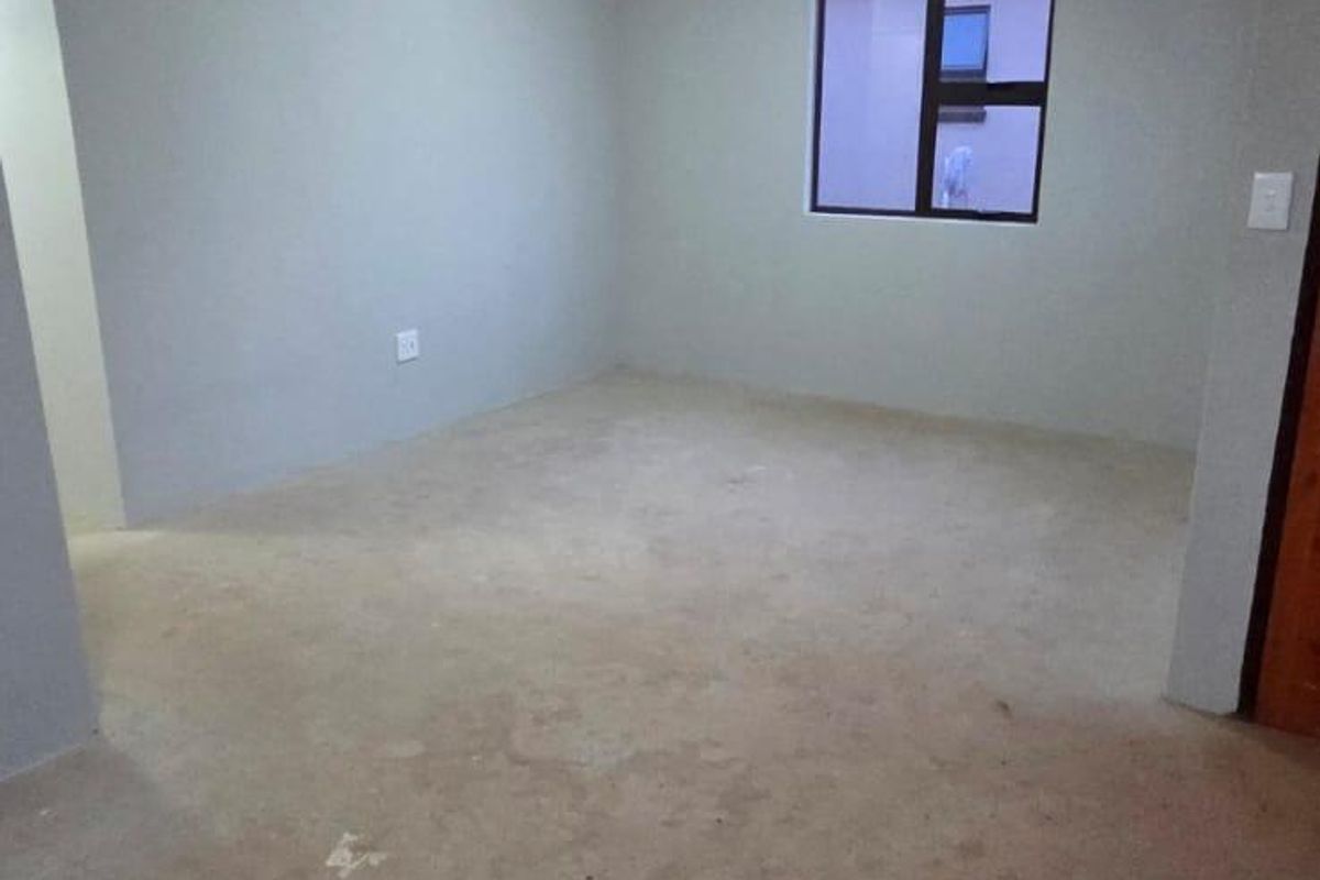 An empty bedroom featuring neutral walls, a ceiling light fixture, and an aluminium window frame, awaiting final flooring installation.