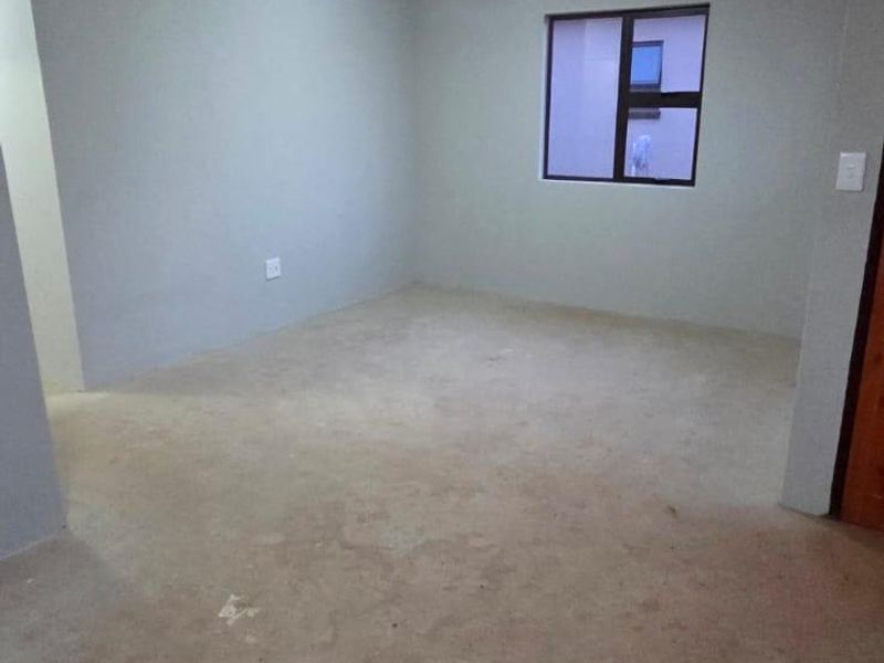An empty bedroom featuring neutral walls, a ceiling light fixture, and an aluminium window frame, awaiting final flooring installation.