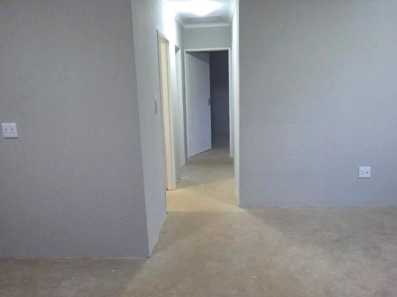 An empty interior hallway featuring grey painted walls, cove cornicing, and unfinished concrete flooring, leading to an adjacent room.