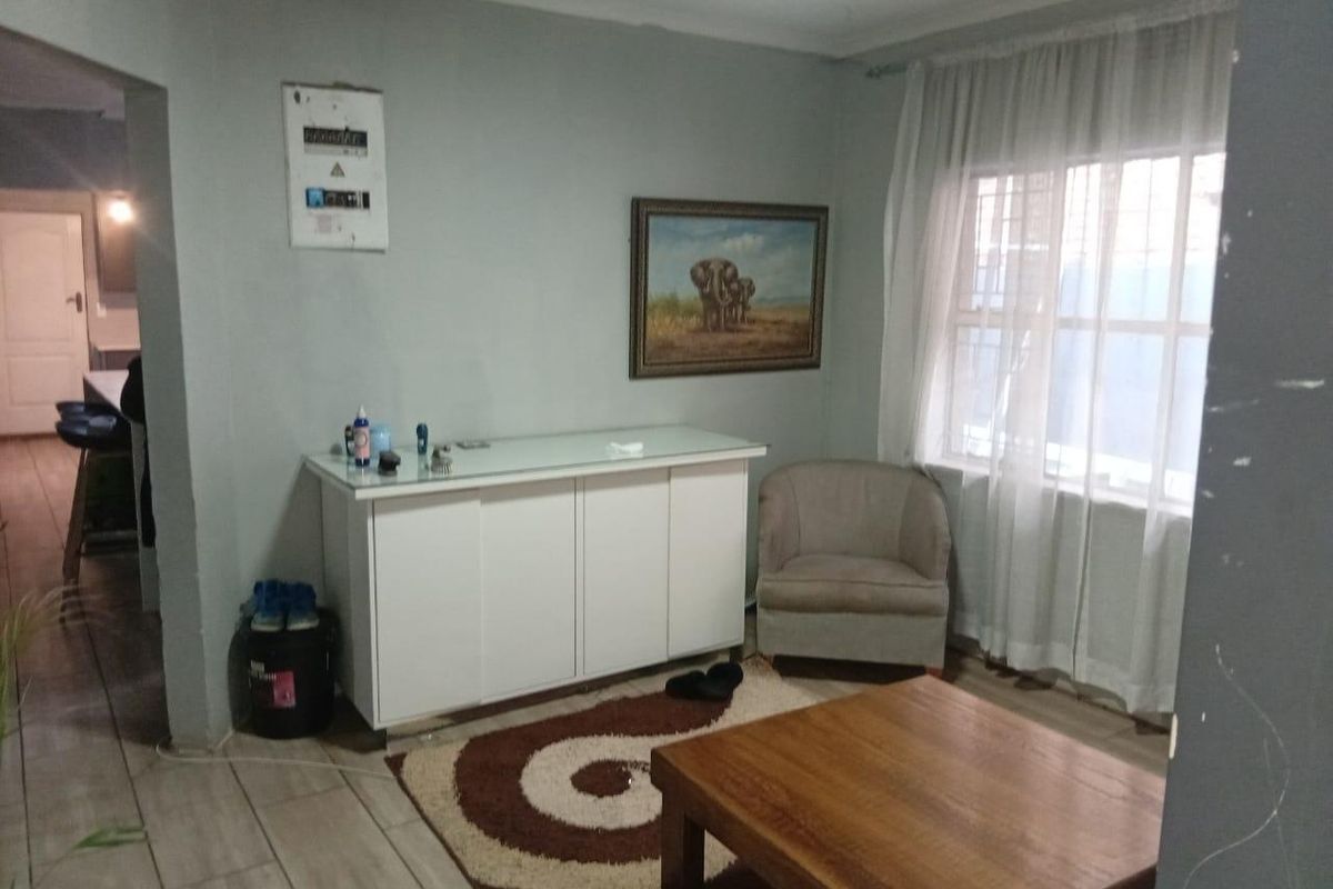 A living room area featuring tiled flooring, a wall-mounted electrical distribution board, and a window with security bars.