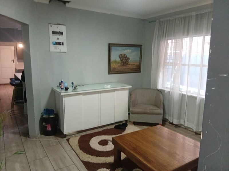 A living room area featuring tiled flooring, a wall-mounted electrical distribution board, and a window with security bars.