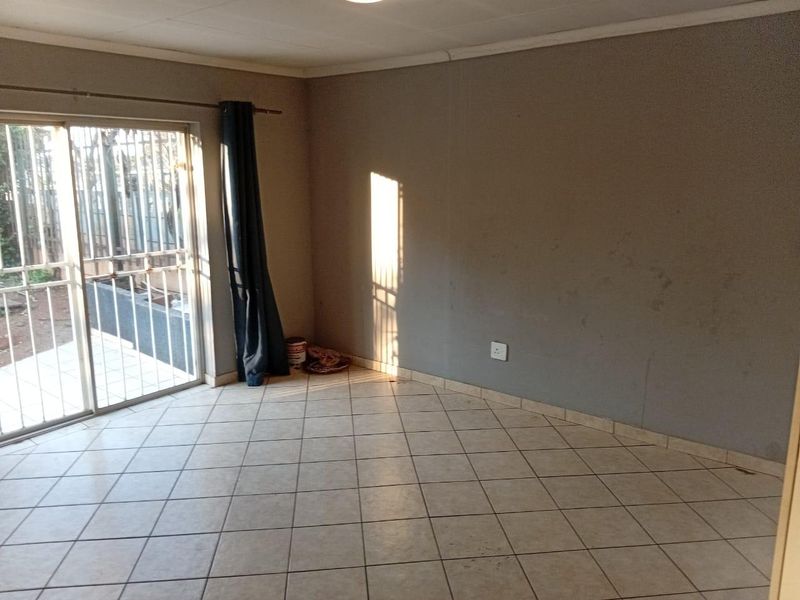 An empty living room featuring tiled flooring and a sliding glass door with security gate, providing access to the exterior.