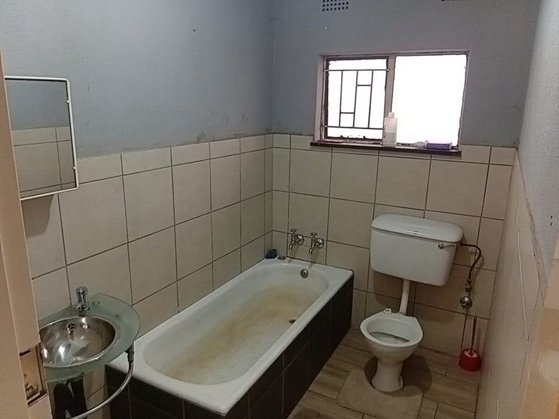 A functional bathroom featuring a bathtub, toilet, and wall-mounted basin with tiled walls and security bars on the window.