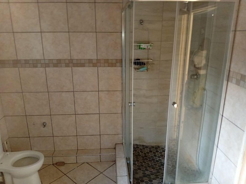 A functional bathroom featuring a glass shower enclosure, tiled walls, and a standard toilet, requiring some maintenance to the tile grout.
