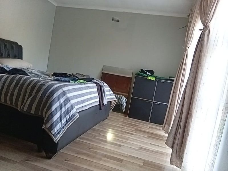 A bedroom featuring light-toned laminate flooring and neutral wall finishes, offering a functional space with natural light from the window.